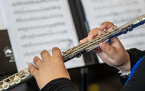 Student plays an instrument in class with other students in the background.