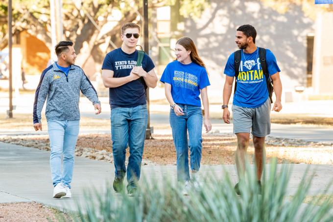 Four Angelo State students walking outside talking and smiling
